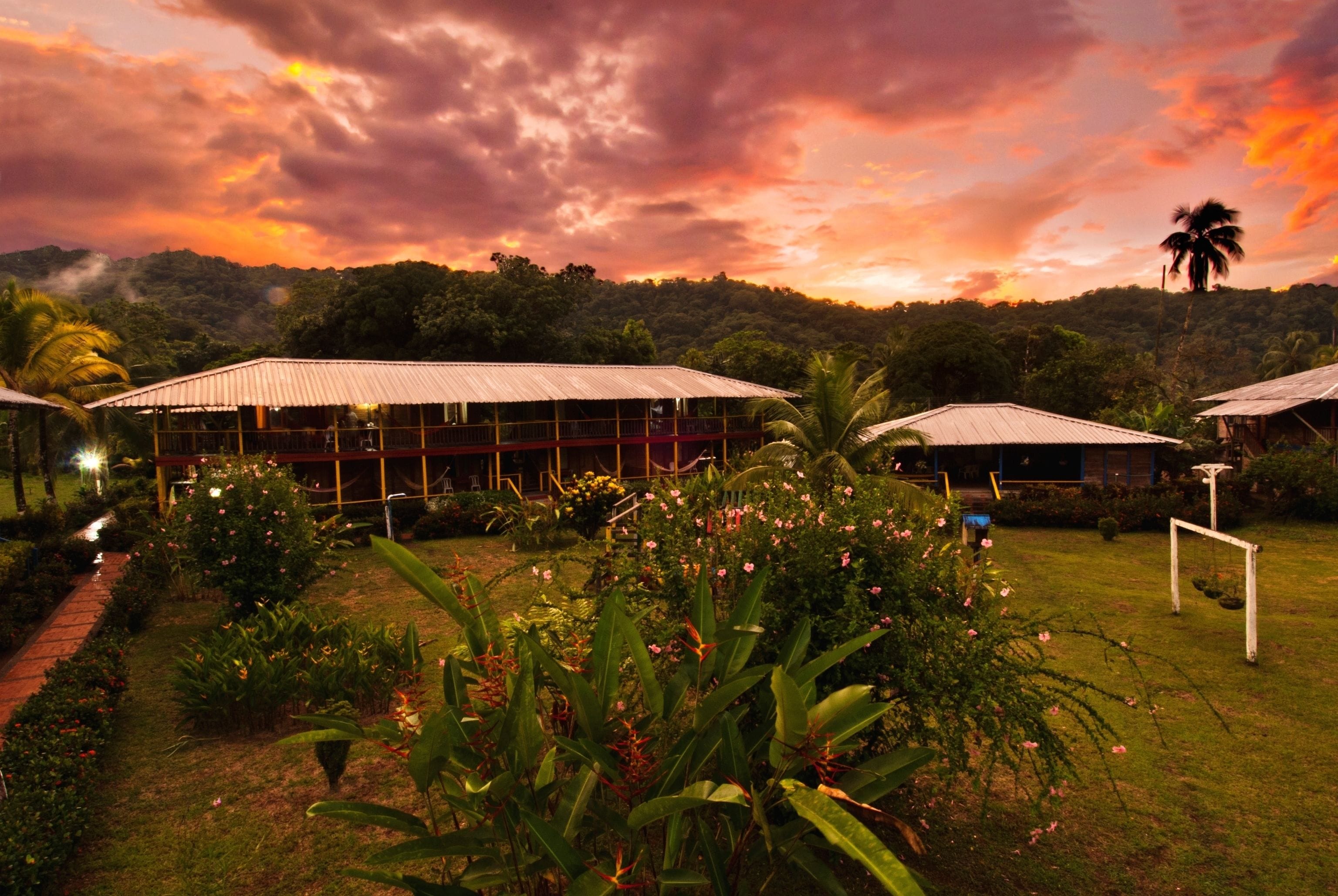 Um resort com vários edifícios, um jardim bem cuidado e vista para uma colina arborizada.