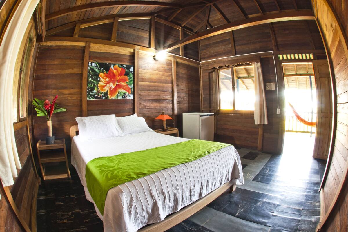 Une pièce en bois avec un lit, une table de chevet, une lampe et une fenêtre avec des rideaux.