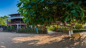 Un hotel de dos pisos, con jardín cercado y zona de playa arenosa.