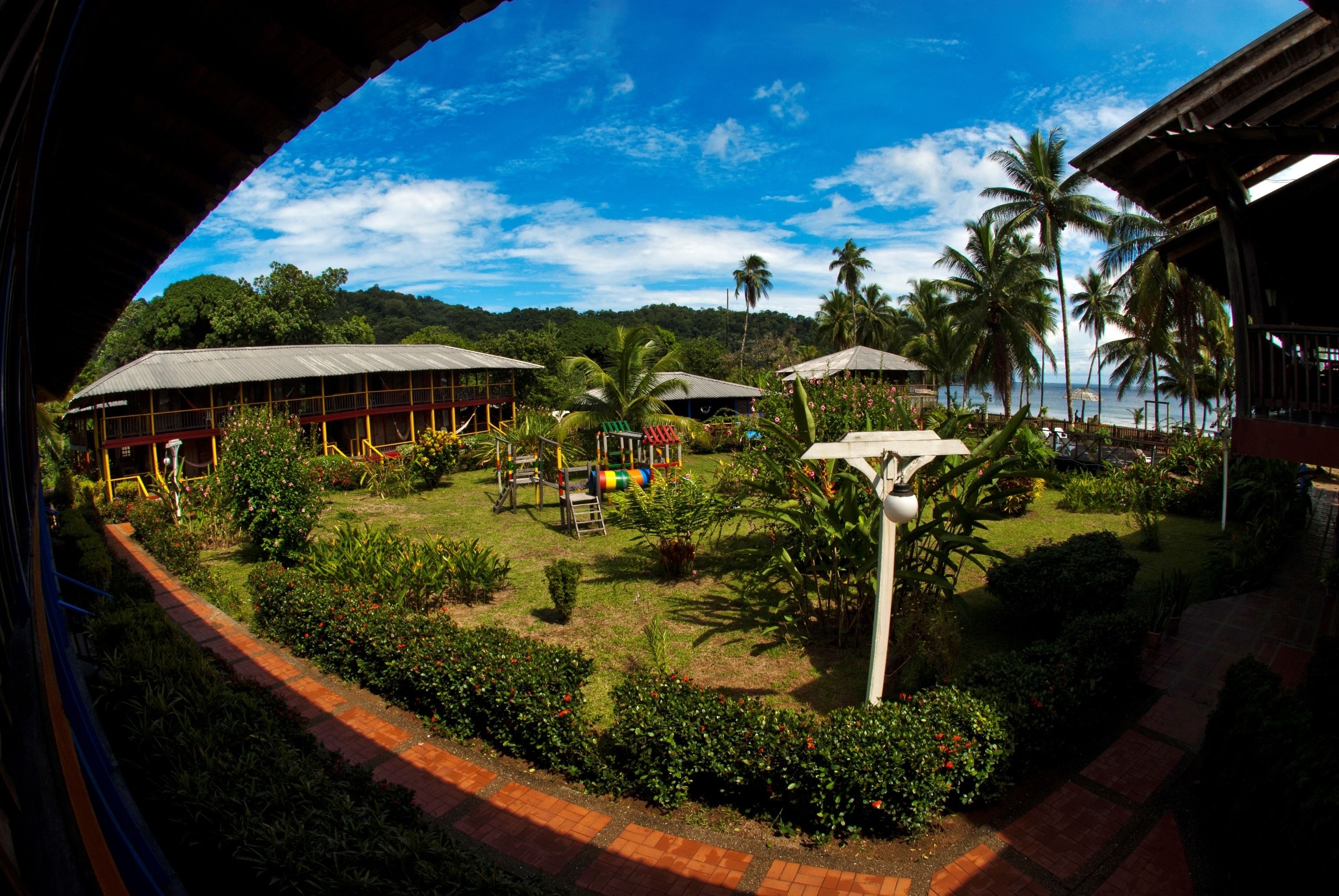 A resort with a covered outdoor area, palm trees, and a view of the ocean.