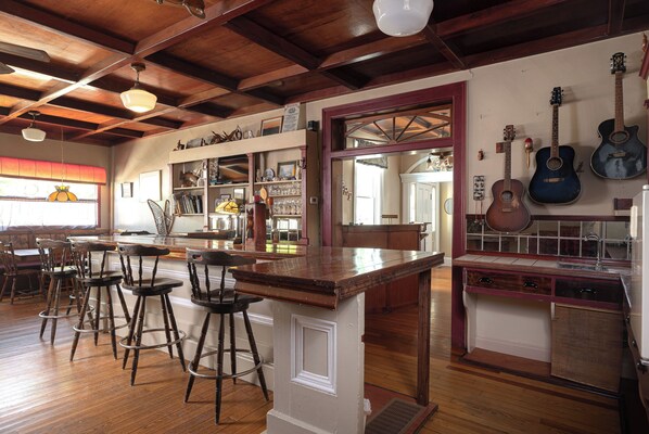 Zona de bar con taburetes de madera, barra y una guitarra colgada en la pared.