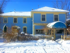 Un edificio de dos pisos con fachada azul y amarilla, una entrada cubierta que dice "Port Albert Inn", y un paisaje cubierto de nieve.