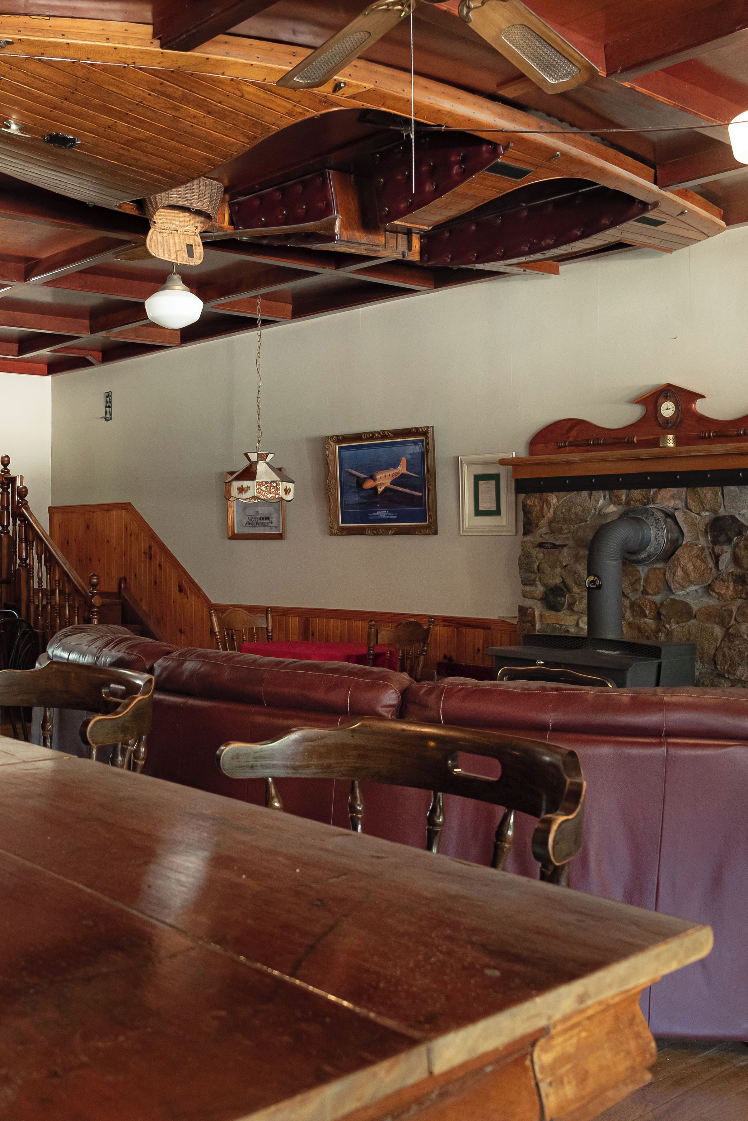 A wooden dining table with chairs, a stone wall with a fireplace, and a wooden ceiling with exposed beams.
