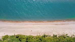 A beach with clear turquoise water, sandy shore, and dense green vegetation in the foreground. - Port Albert Inn (Ashfield-Colborne-Wawanosh)