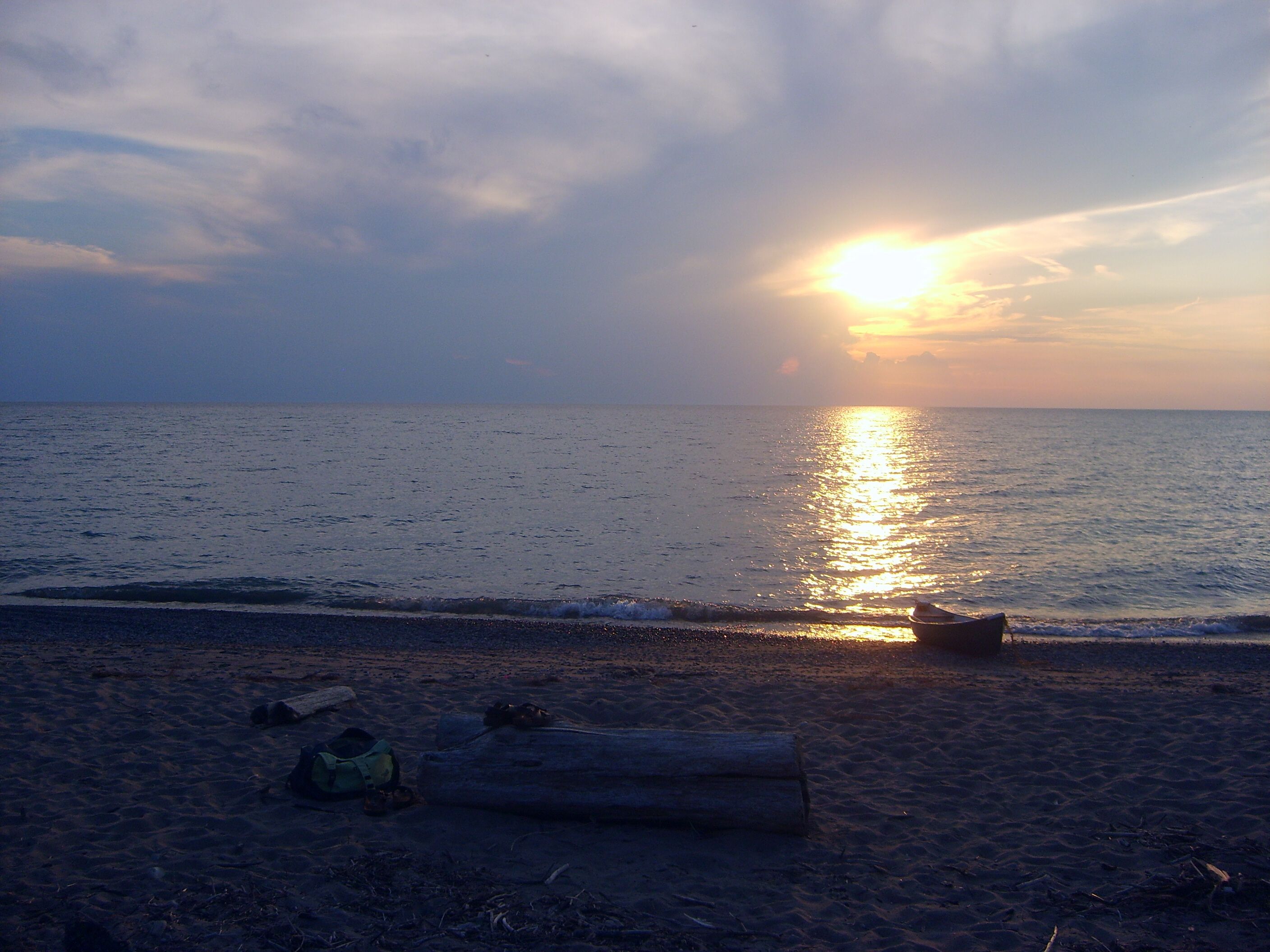 Une plage avec un bateau, une bûche et un sac à dos sur le sable.