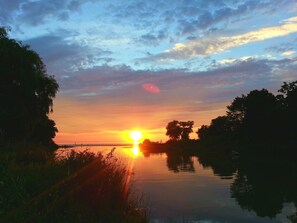 Un atardecer sobre aguas tranquilas, flanqueado por árboles a ambos lados.