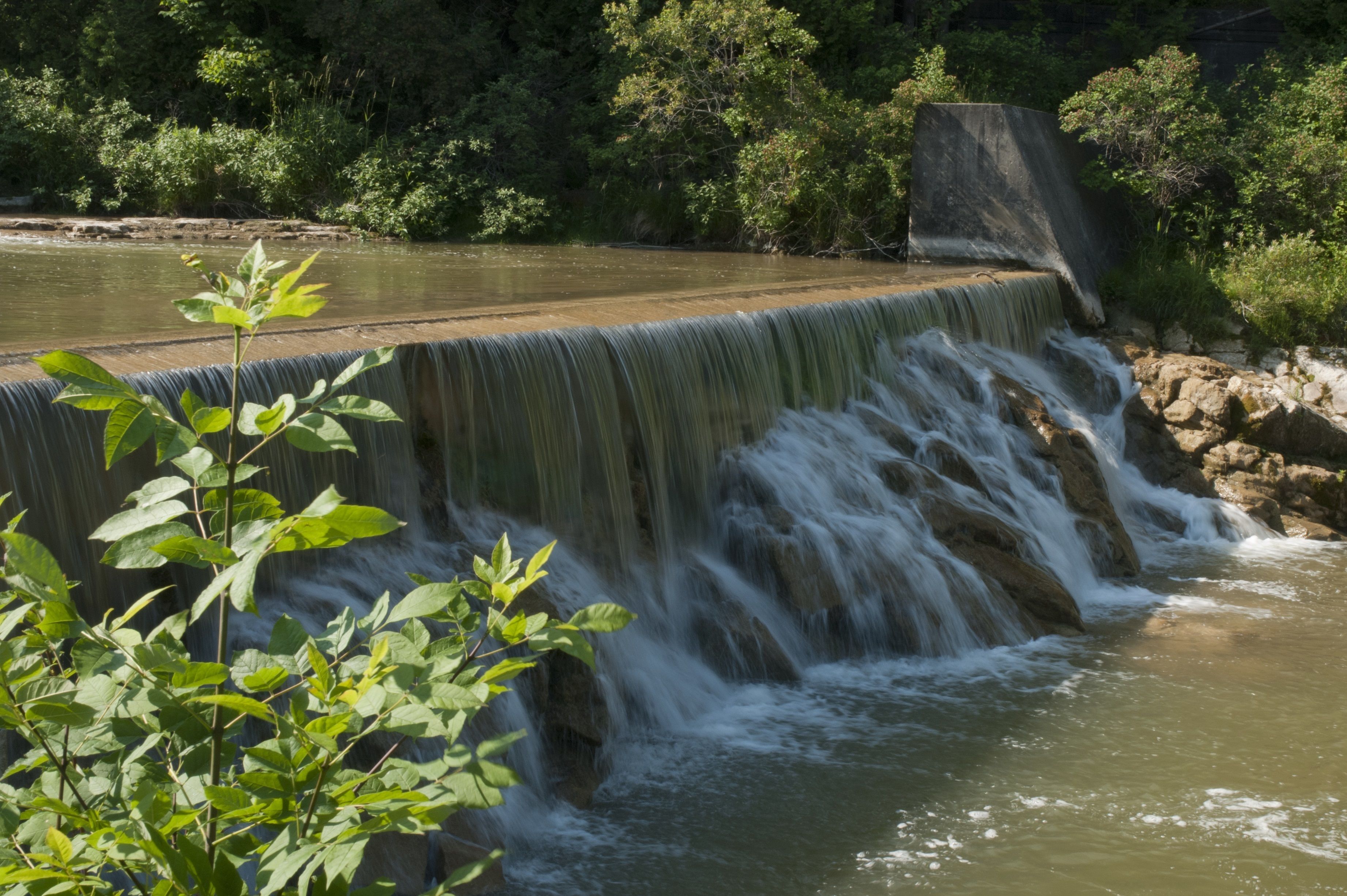 Un barrage avec une cascade, entouré de verdure.