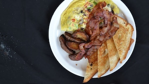 Een bord met een omelet, spek, toast en geroosterde aardappelen.