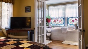 Een kamer met een bed, een televisie, een badkamer met een bad en een raam met glas-in-lood.