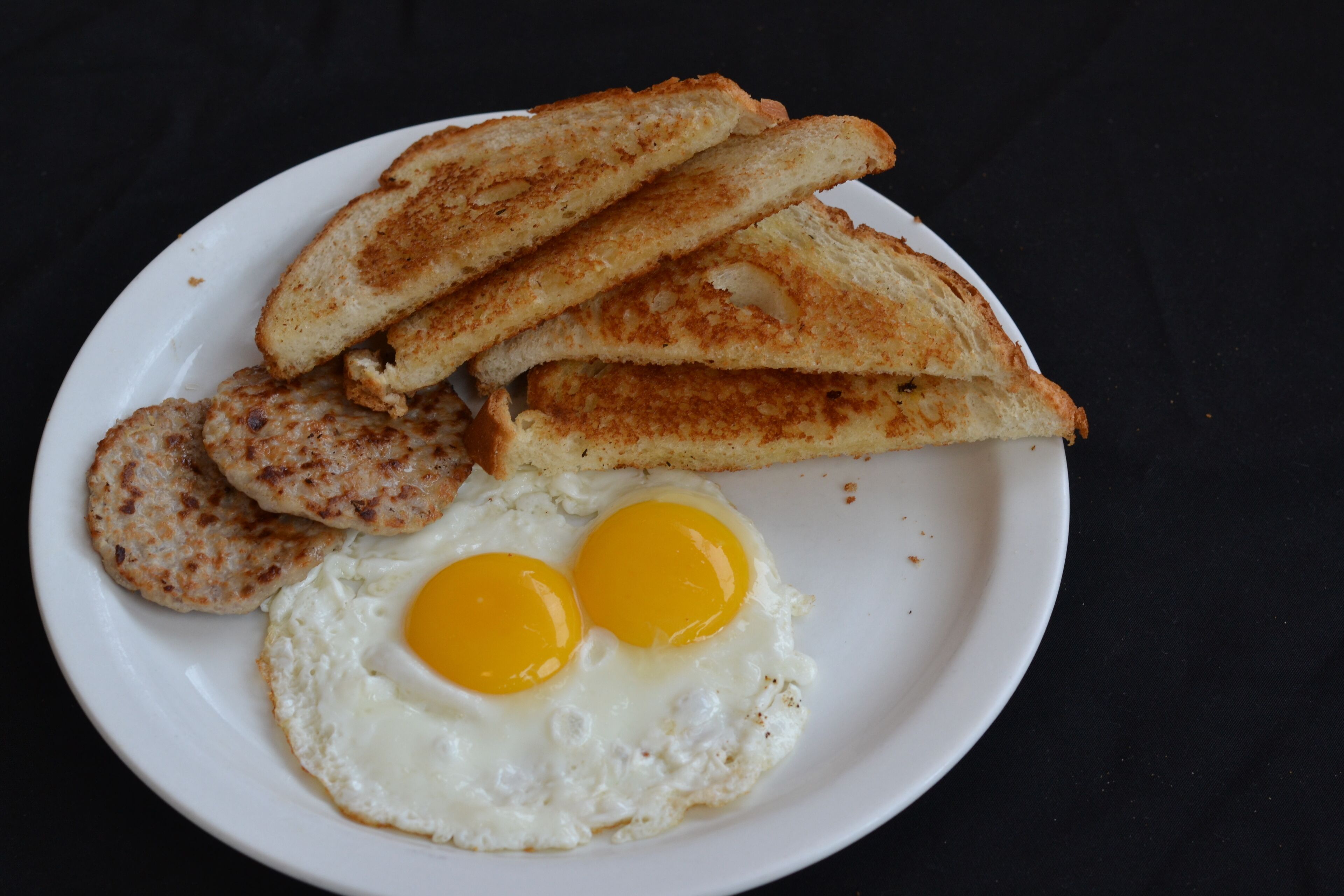 A plate with two fried eggs, two slices of toast, and two sausage patties.