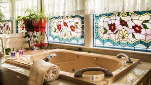 Een badkamer met een ruime badkuip, een spiegel en een raam met glas-in-lood.