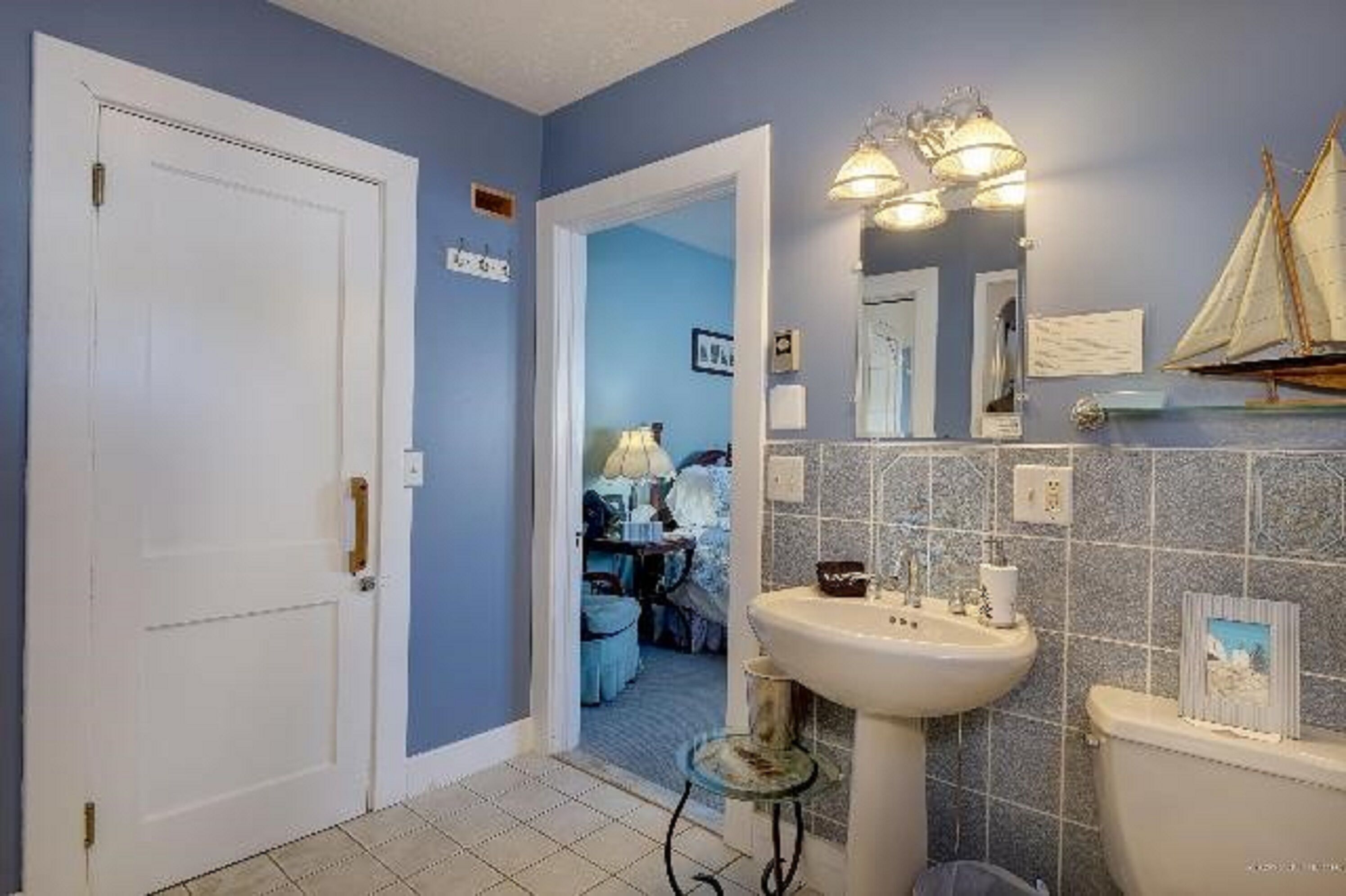 A bathroom with a sink, mirror, and a small ship model on the wall.