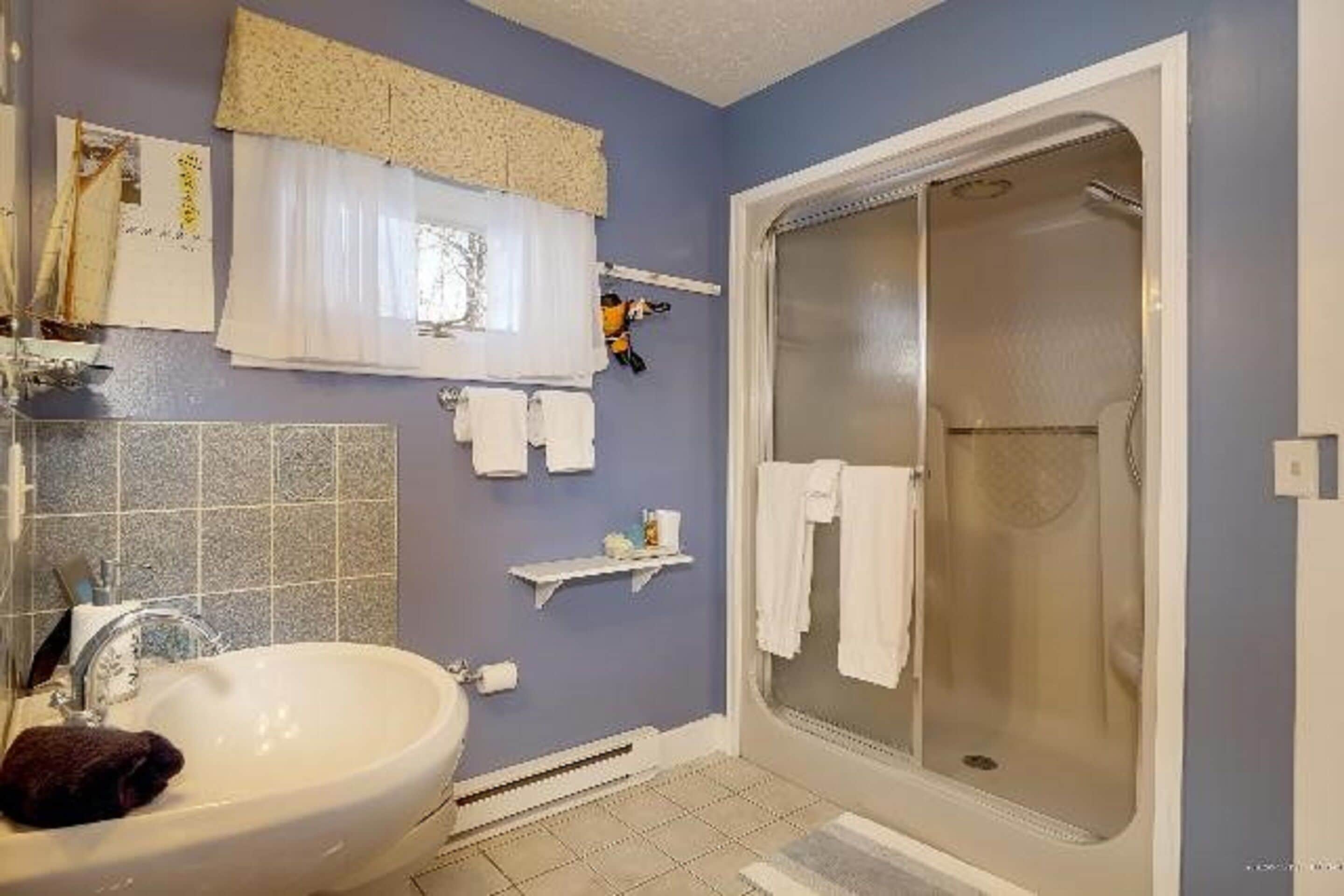 Un baño con lavamanos, espejo, toallero, ducha y paredes con azulejos.