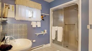 Un baño con lavamanos, espejo, toallero, ducha y paredes con azulejos.