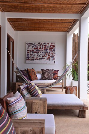 A hammock chair, a wooden bench, and a sofa with colorful cushions in a room with a woven ceiling and a large abstract painting on the wall. - OITI by Barracuda (Itacaré)