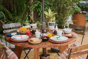 Une table ronde en bois, dressée pour le petit-déjeuner, entourée de chaises et de plantes en pot.