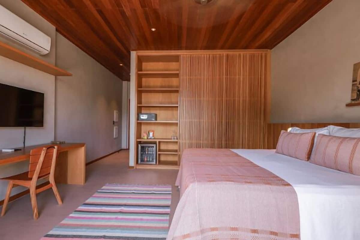 Een moderne slaapkamer met een houten plafond, een bed met roze beddengoed, een bureau met stoel, een televisie en een inbouwkast.