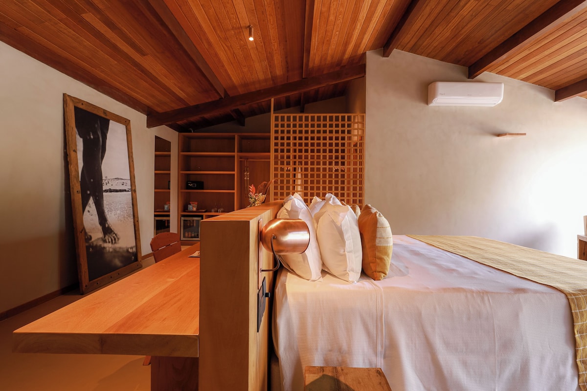 Een slaapkamer met een houten plafond, een bed met wit beddengoed, een houten tafel en een groot, ingelijst schilderij aan de muur.
