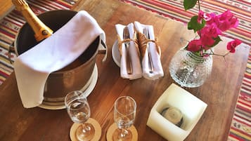 Una mesa de madera con una botella de champán, dos copas de vino, un florero con flores rosas y un candelabro.
