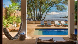 Un área junto a la piscina con sillas de descanso, una hamaca y vista al mar.