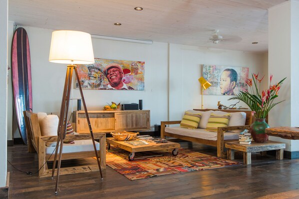 Uma sala de estar acolhedora com um sofá de madeira, uma luminária de chão, uma mesa de centro e uma prancha de surf encostada na parede.