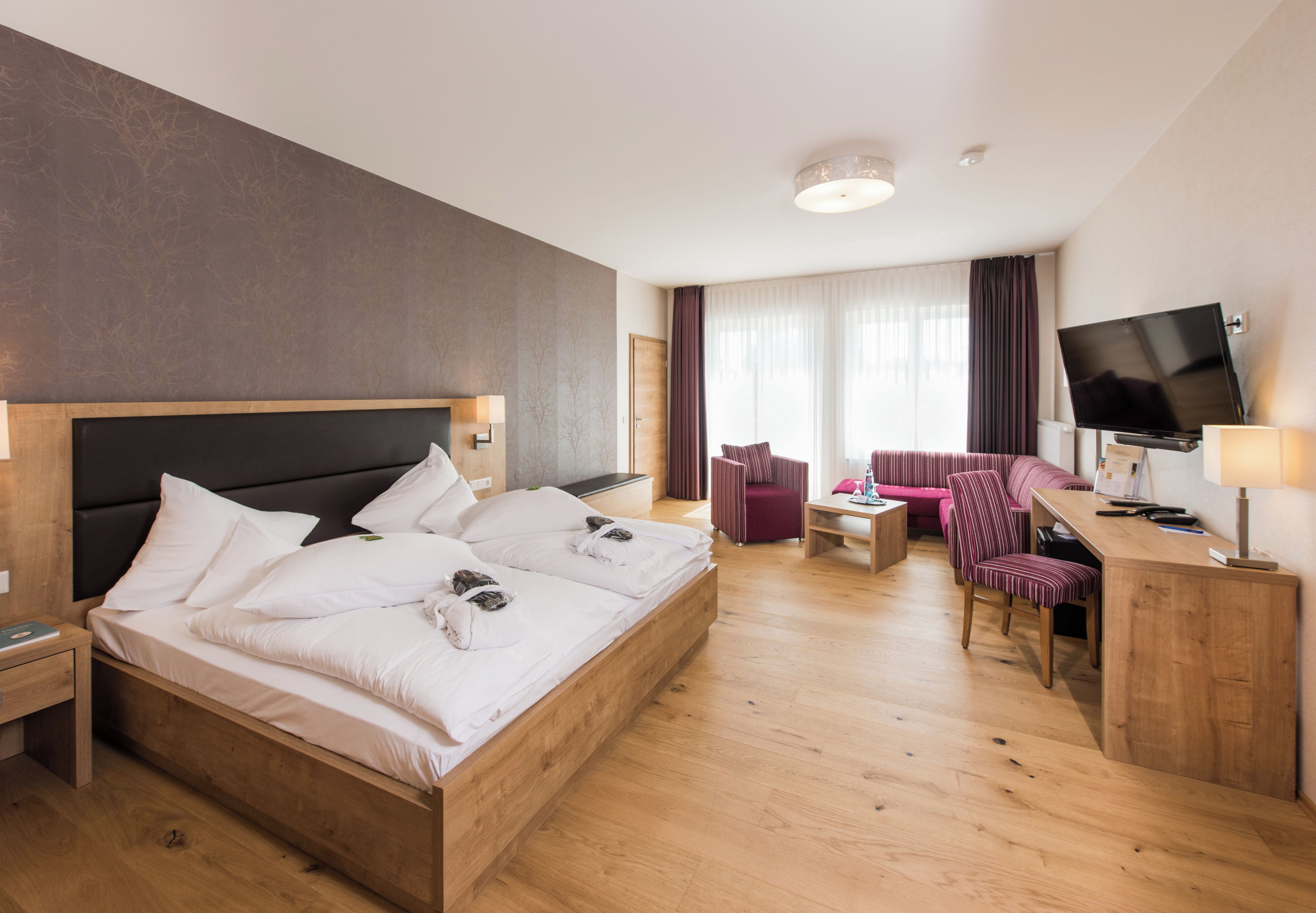 A hotel room with a large bed, a desk with a TV, a chair, a small table, and a sofa.