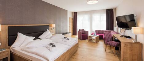 A hotel room with a large bed, a desk with a TV, a chair, a small table, and a sofa.