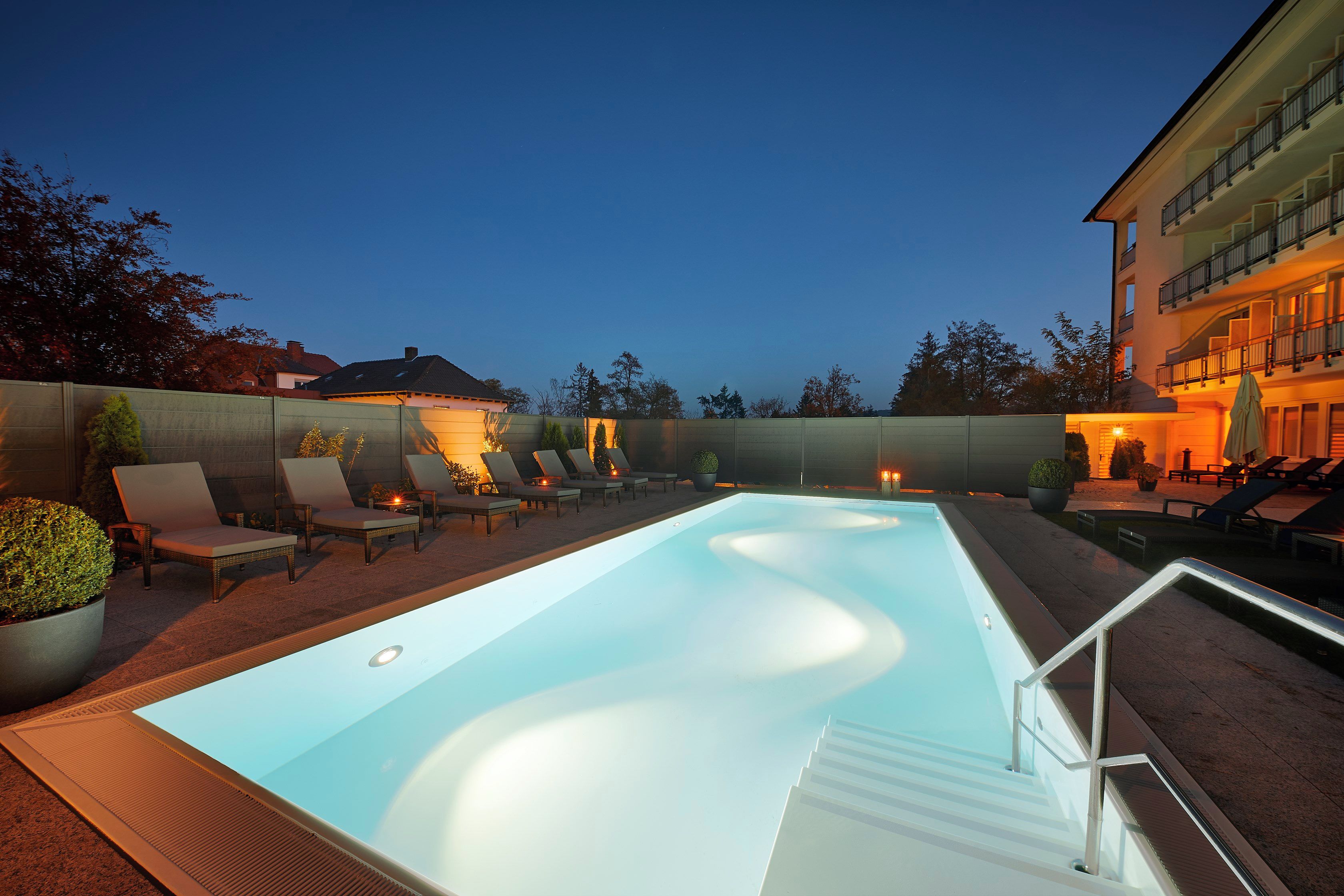 Ein Schwimmbecken mit Liegestühlen und einem Gebäude im Hintergrund.