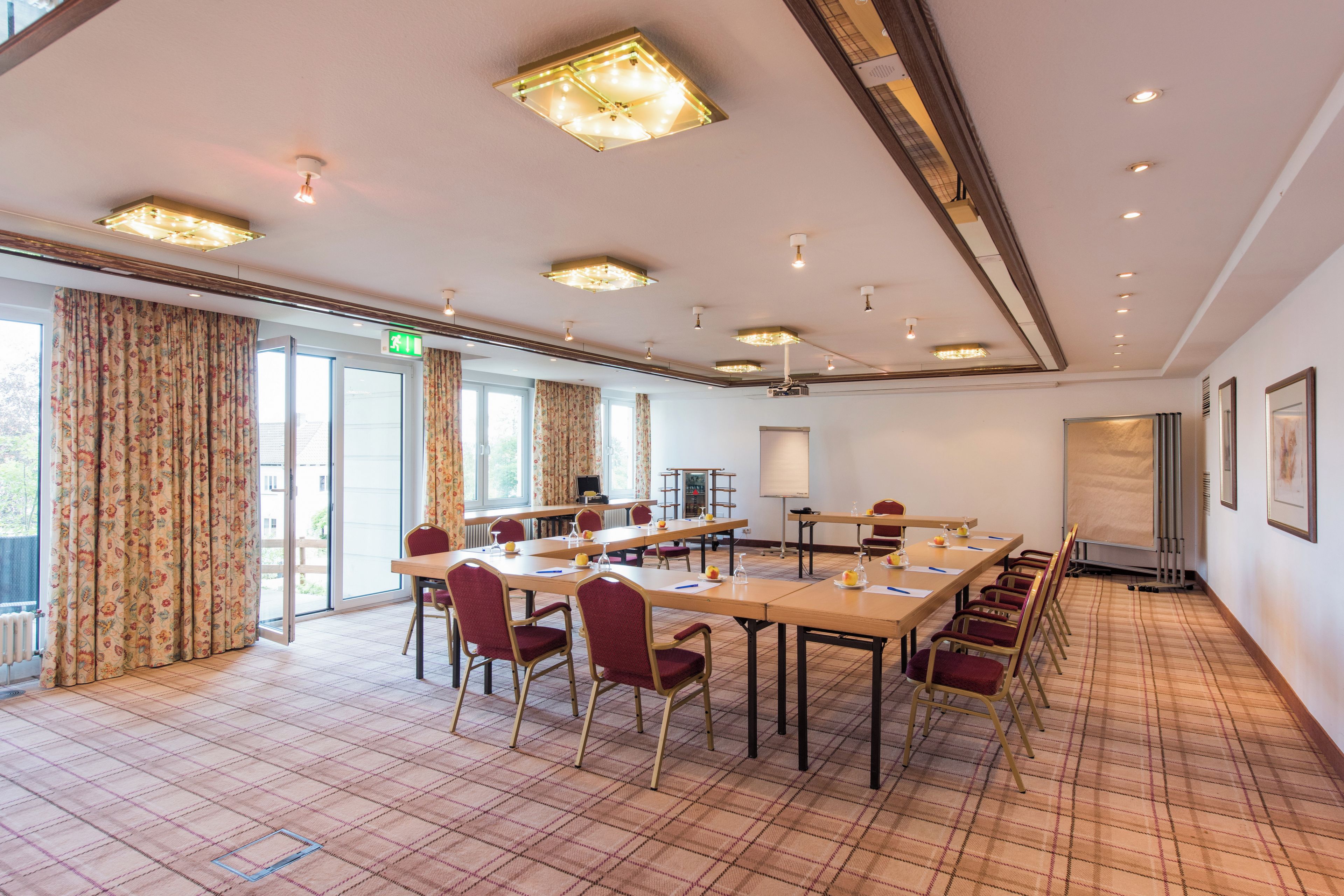 A conference room with a long table, chairs, a projector screen, and a large window with curtains.