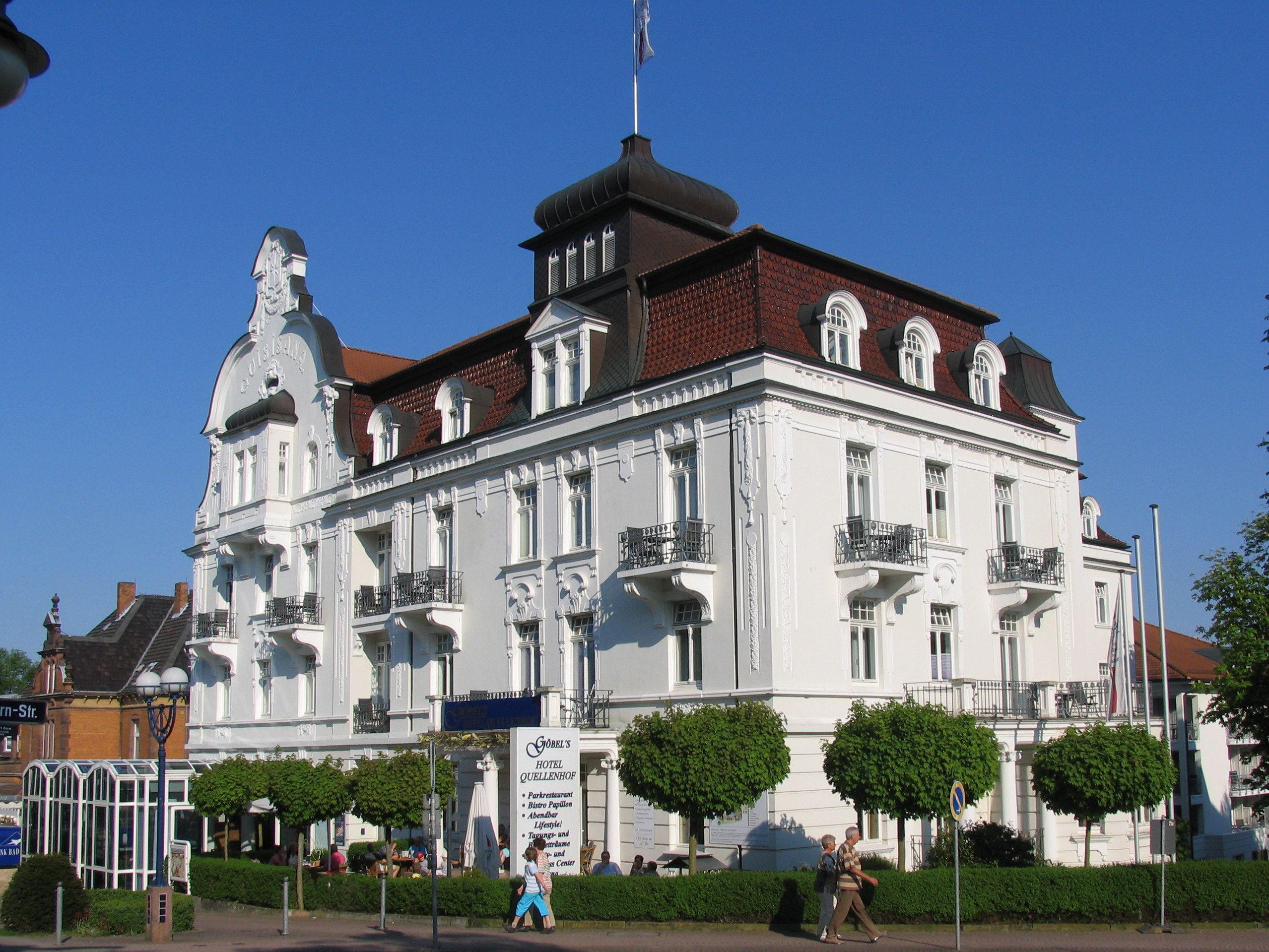 A historic building with a prominent clock tower, multiple balconies, and a sign indicating it is a hotel.