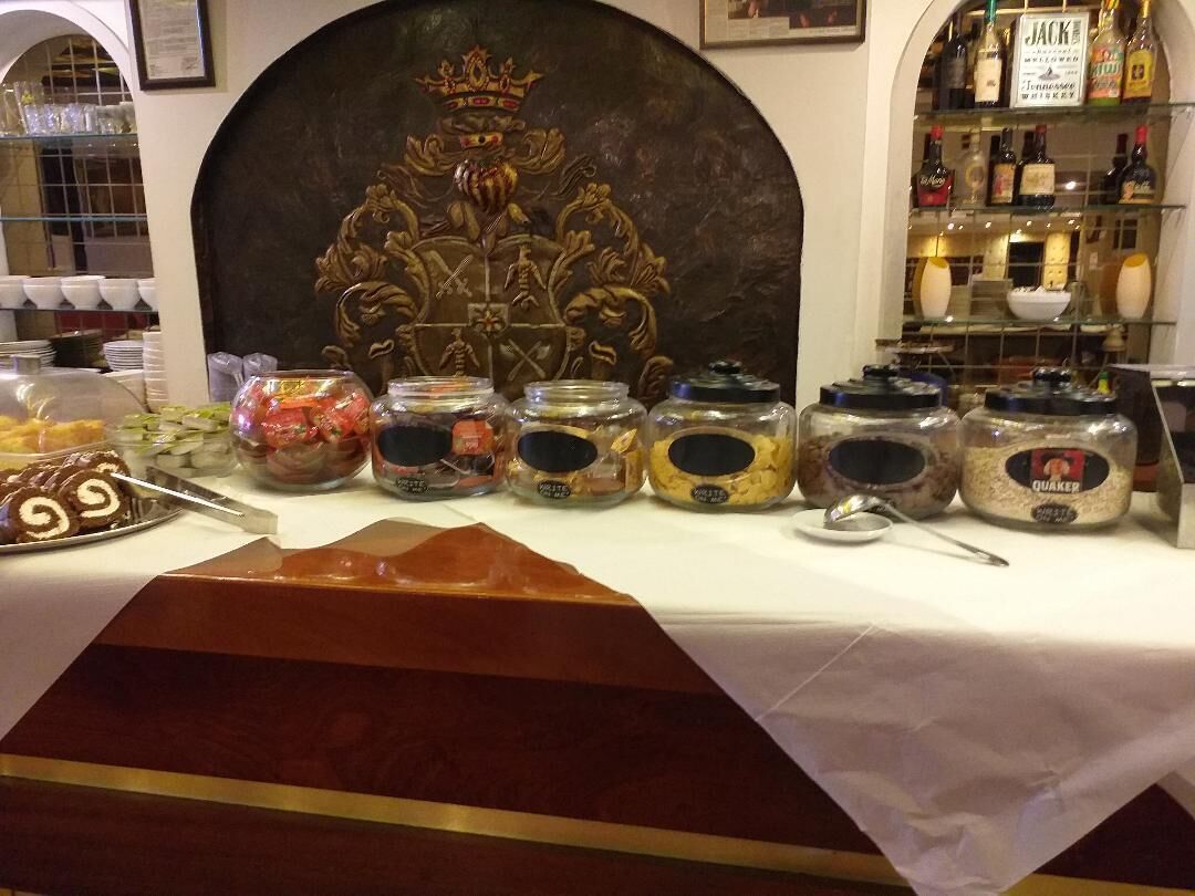 Una mesa de buffet con diferentes alimentos y salsas, una pared decorativa con un motivo de corona y una selección de botellas de licores.
