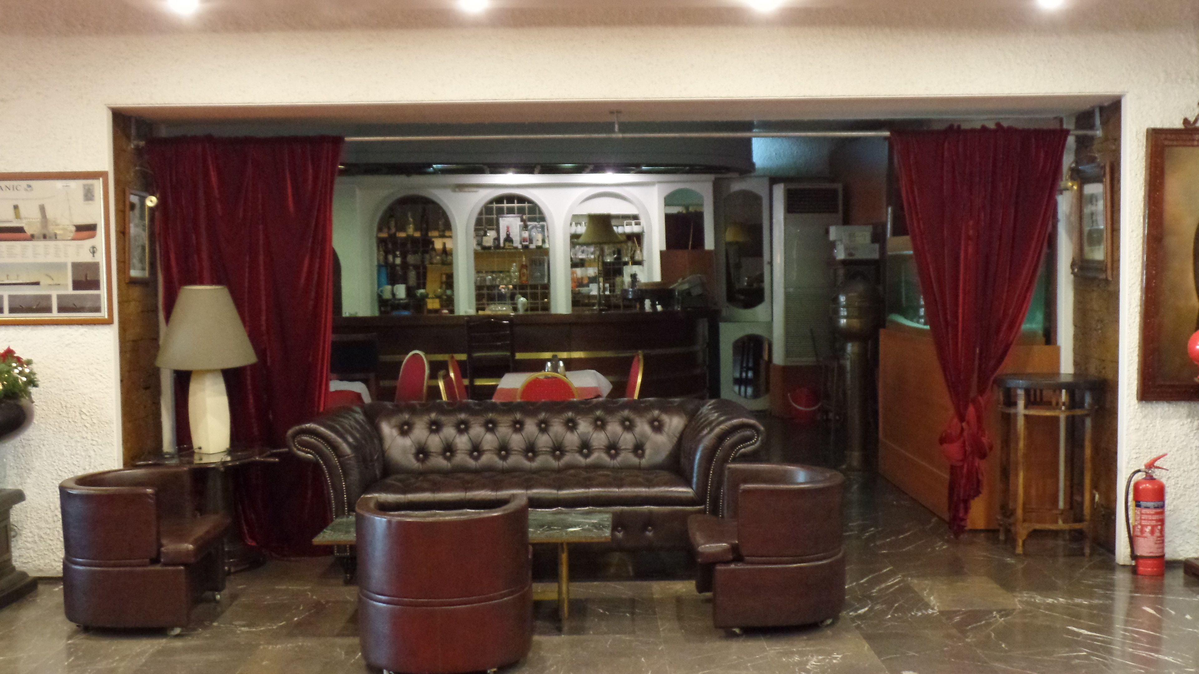 Een ontvangsthal met een leren bank, fauteuils, een bar met planken, en een brandblusser.