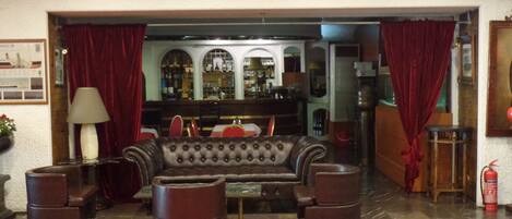 A lobby with a leather sofa, armchairs, a bar area with shelves, and a fire extinguisher.