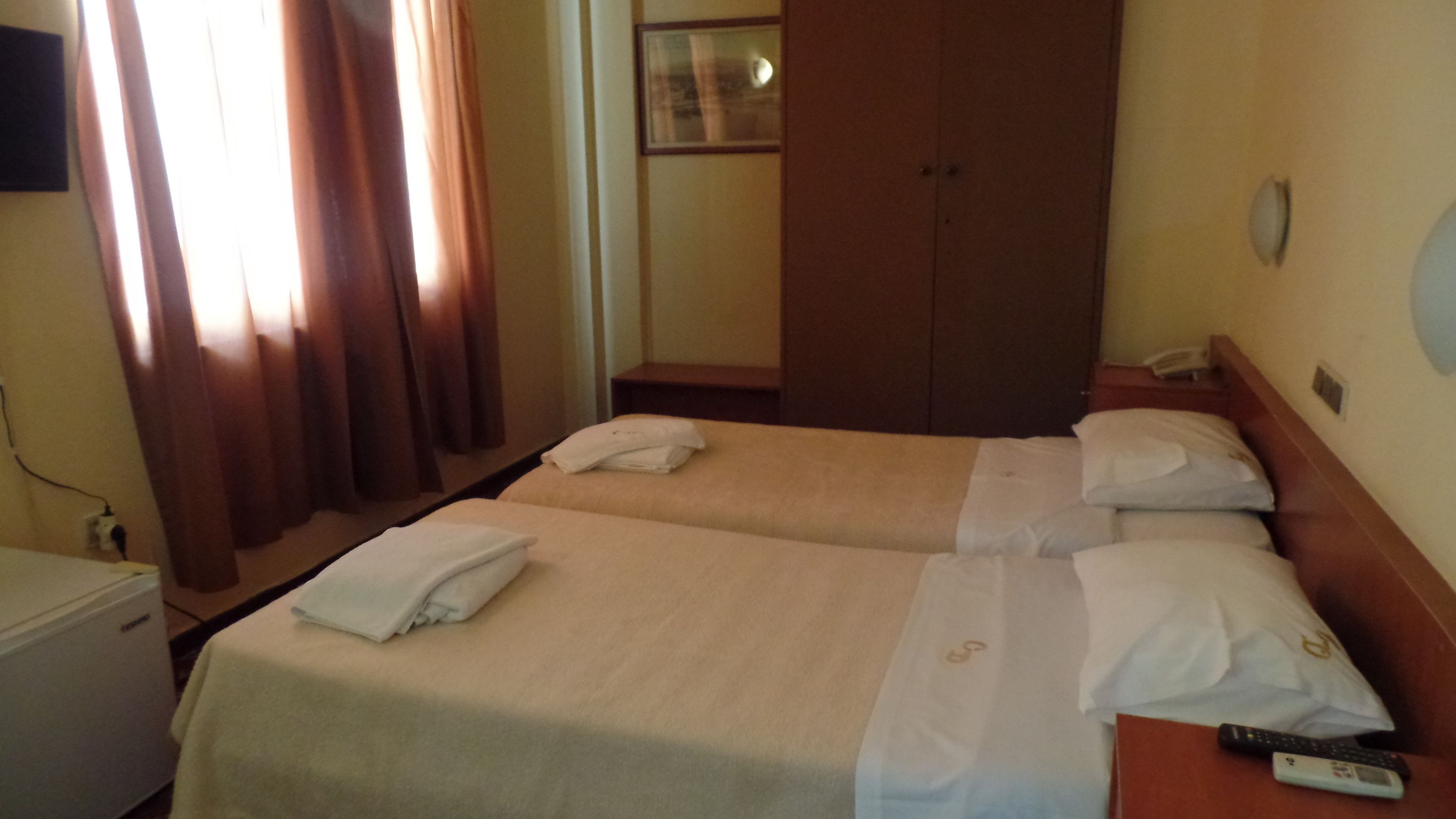 Habitación de hotel con dos camas, un armario, un escritorio y una televisión.