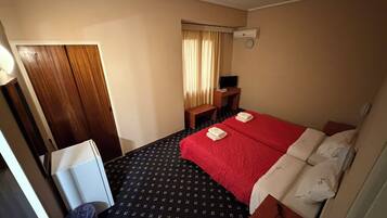 Habitación de hotel con cama, escritorio, silla, televisor y aire acondicionado.