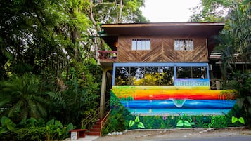 Un edificio con un mural colorido de una playa, fachada de madera y un balcón.