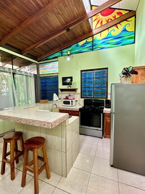 A kitchen with a tiled island, wooden stools, a stove, a microwave, and a refrigerator.