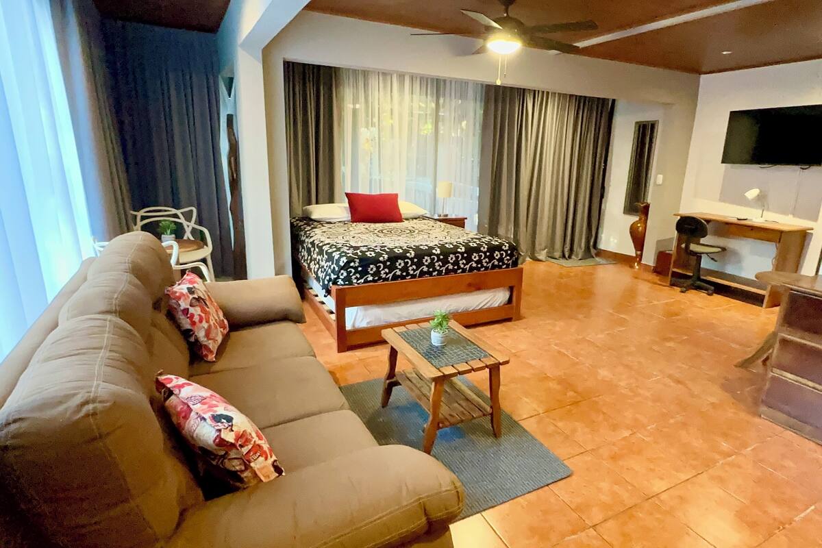 Une chambre d’hôtel avec un lit, un canapé, une petite table, un bureau et un téléviseur.