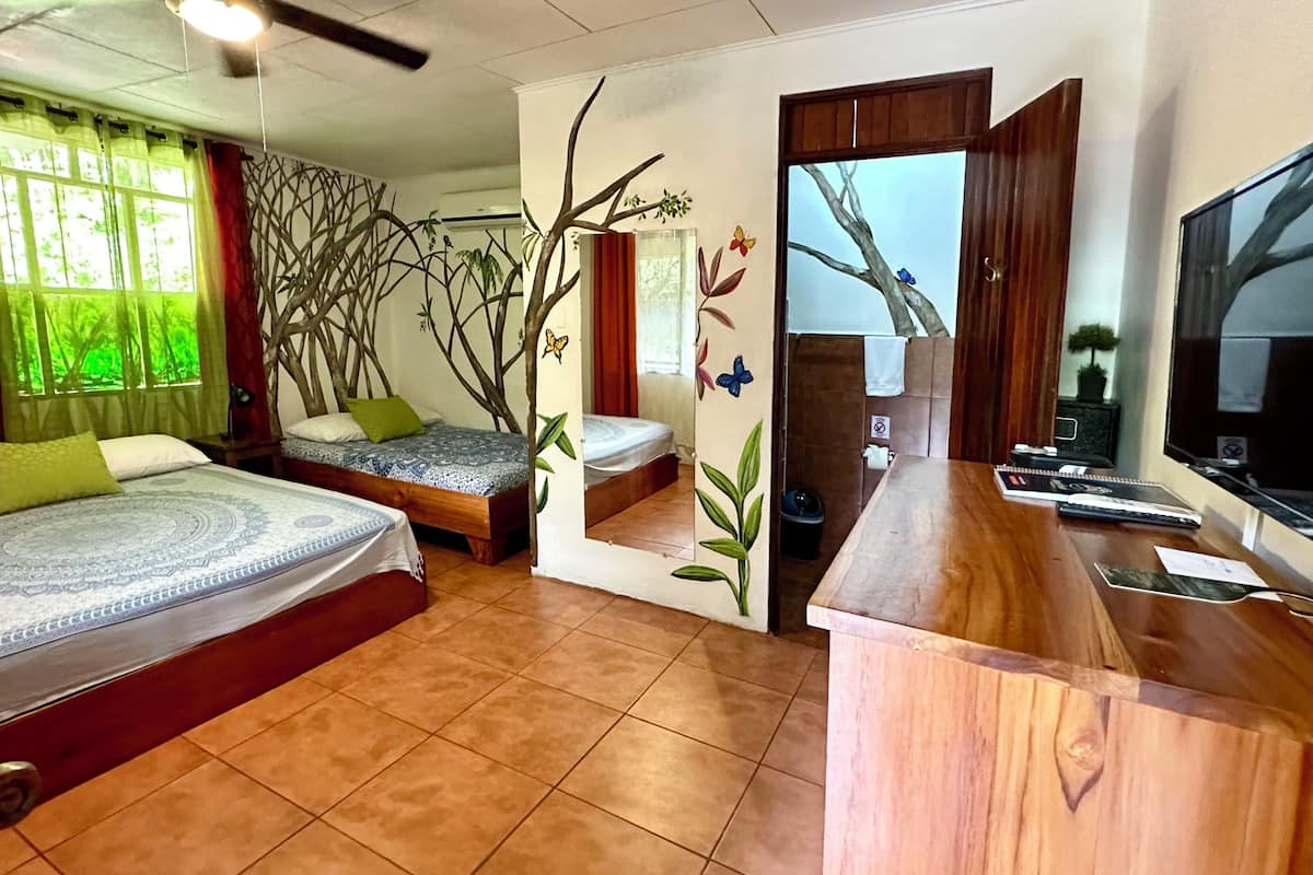 Une chambre d’hôtel avec deux lits, un bureau en bois, une télévision et une salle de bain visible à travers une porte.