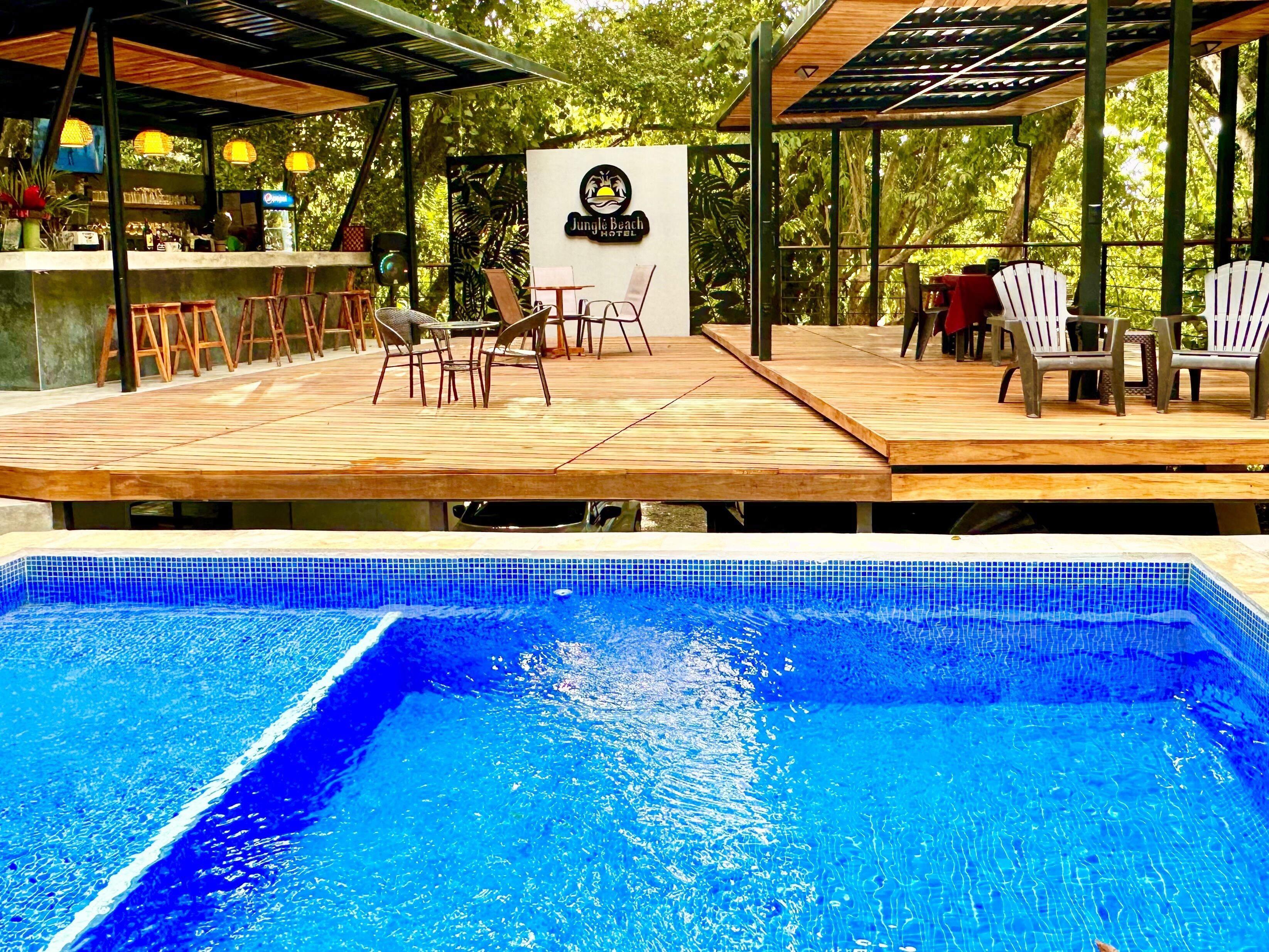 A poolside area with a wooden deck, lounge chairs, and a bar.