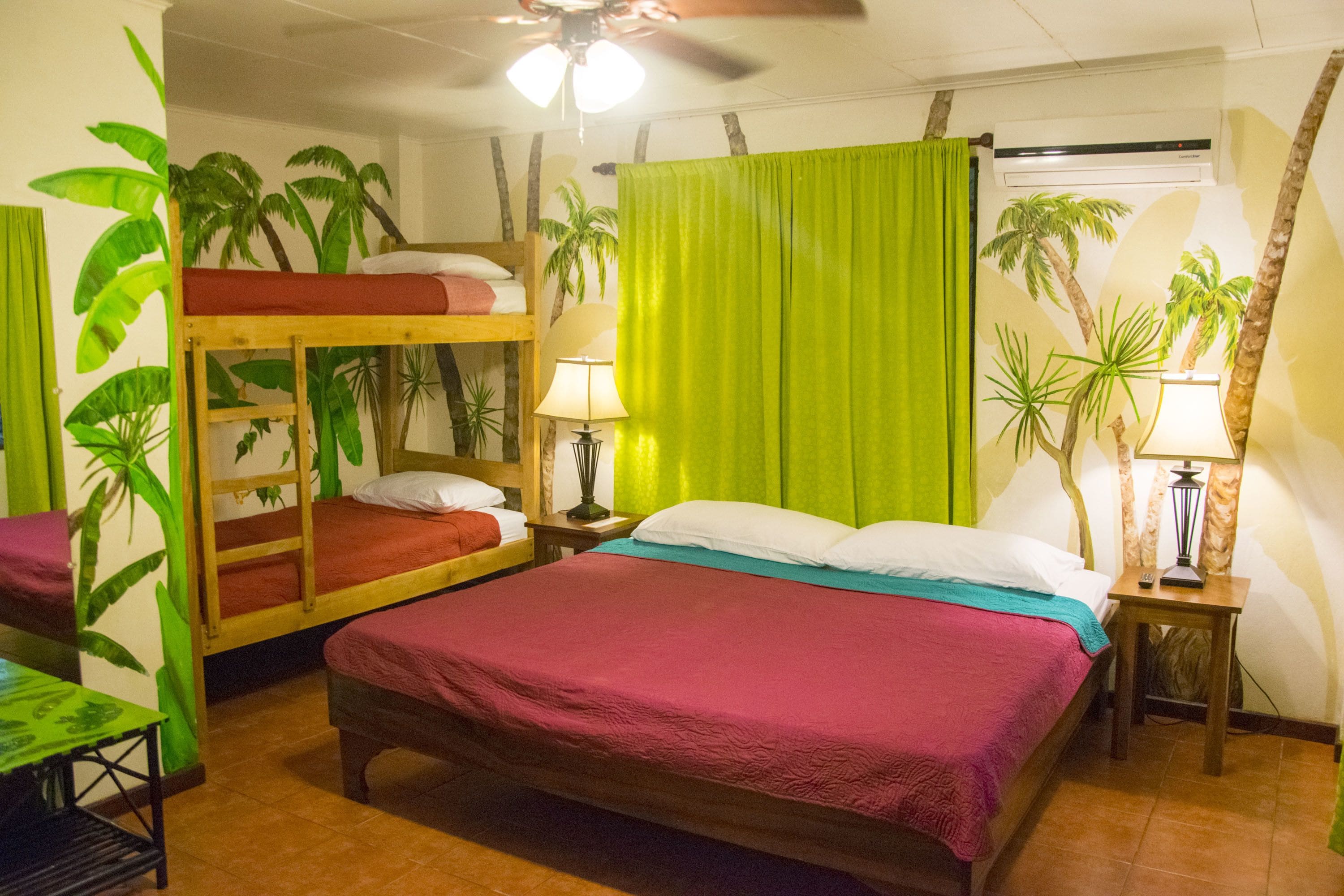 Una habitación con una cama litera, una cama individual, un ventilador de techo y una ventana con cortinas.