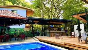 Une piscine avec une terrasse en bois, un espace salon extérieur et un bar.