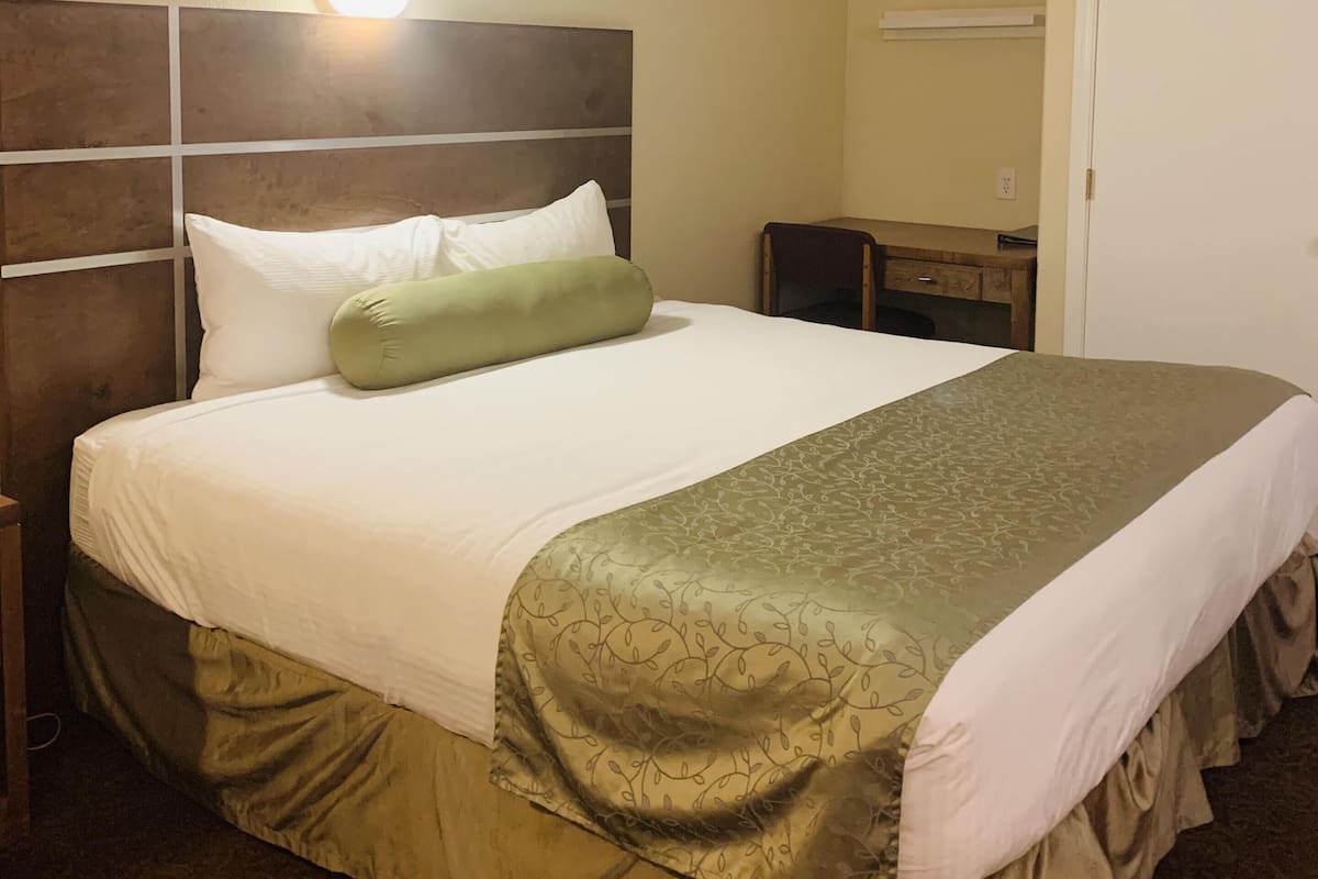 A hotel room with a large bed, a nightstand, a dresser, and a wall-mounted light.