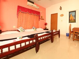Un dormitorio con cama de madera, una cortina roja, una puerta de madera, una mesita con mantel a cuadros y un aire acondicionado de pared.