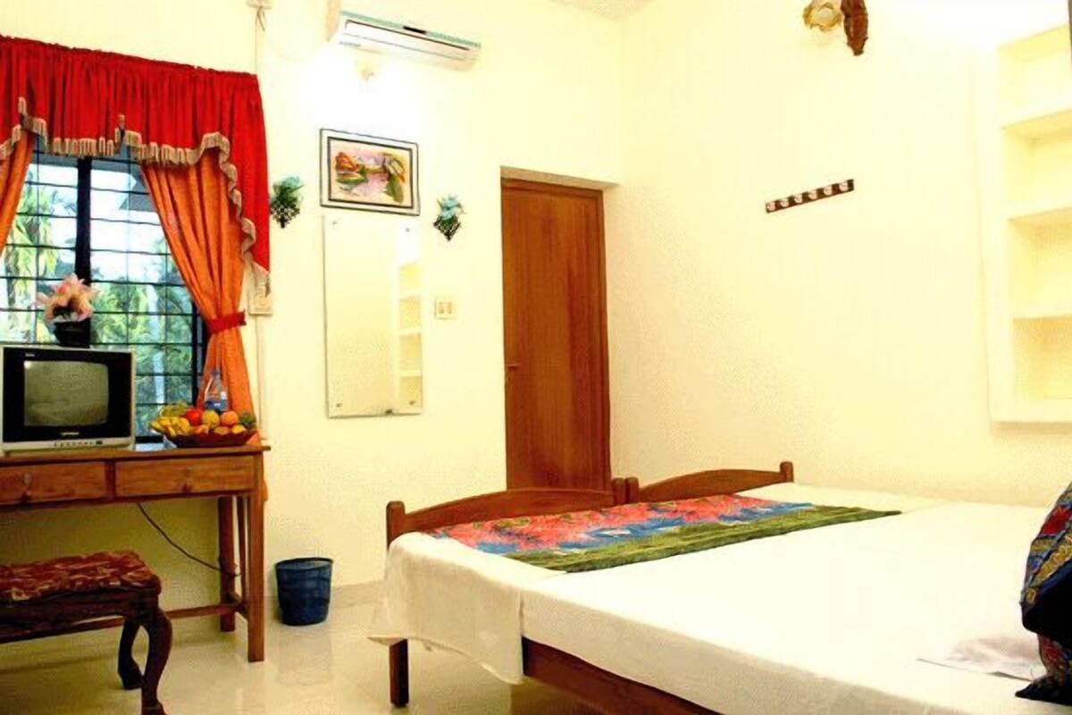 A bedroom with a bed, a desk with a television, and a window with curtains.