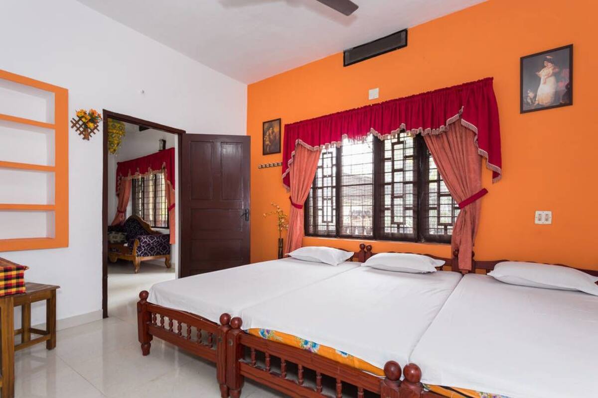 A room with a large bed, orange walls, and a window with red curtains.