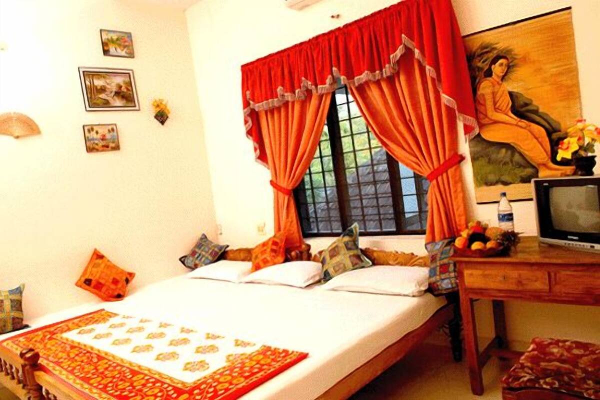 A bedroom with a bed, a wooden desk, a television, and a window with red curtains.