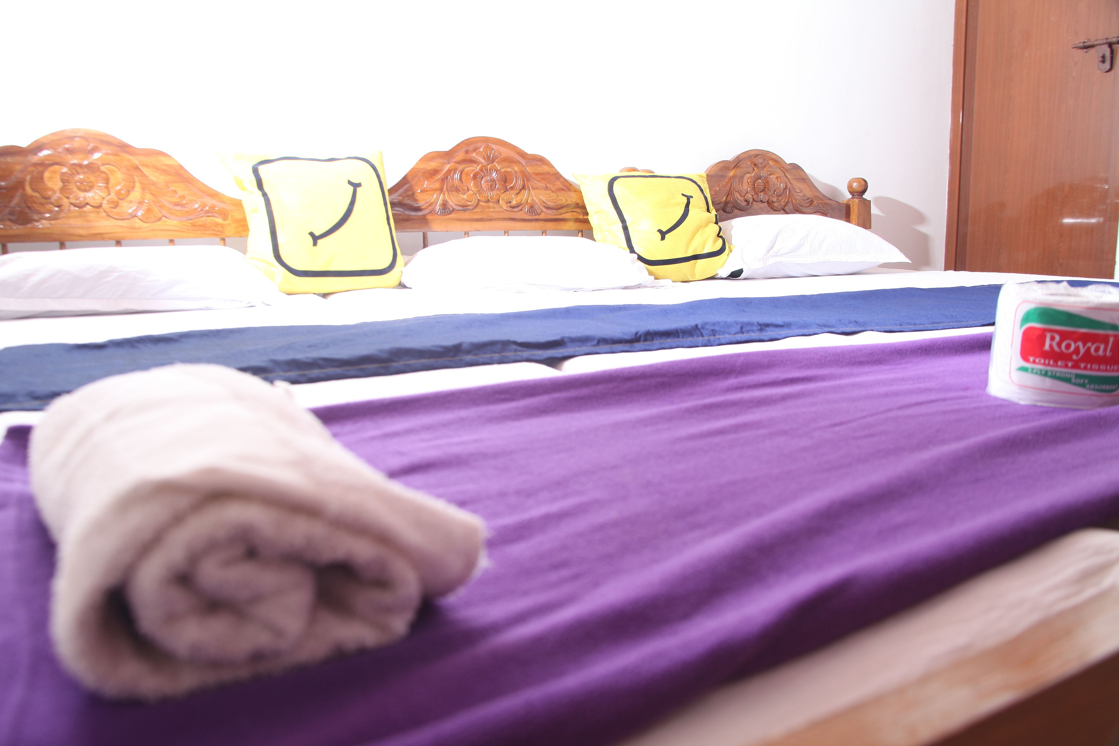 A bed with a purple blanket, a rolled towel, and pillows with smiley faces.