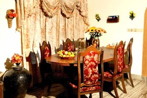 A dining area with a round table, floral-patterned chairs, a vase with flowers, and a fruit bowl.