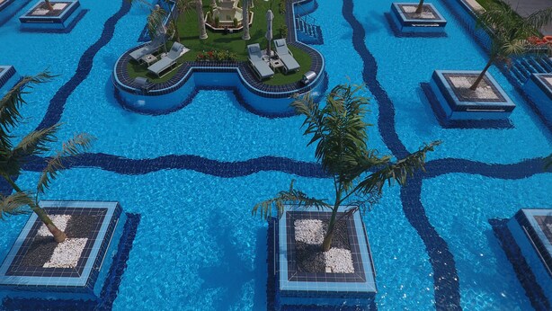 Una gran piscina con múltiples carriles, rodeada de palmeras y sillones de descanso.